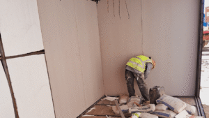Worker in safety gear installs wall panels indoors.