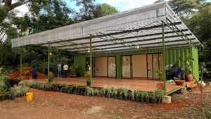 A green container home with a wooden deck and landscaping.
