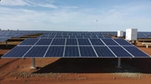 Large array of solar panels on red soil under a blue sky.