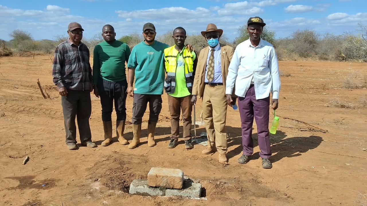 Group of six men at a construction site with a stone.