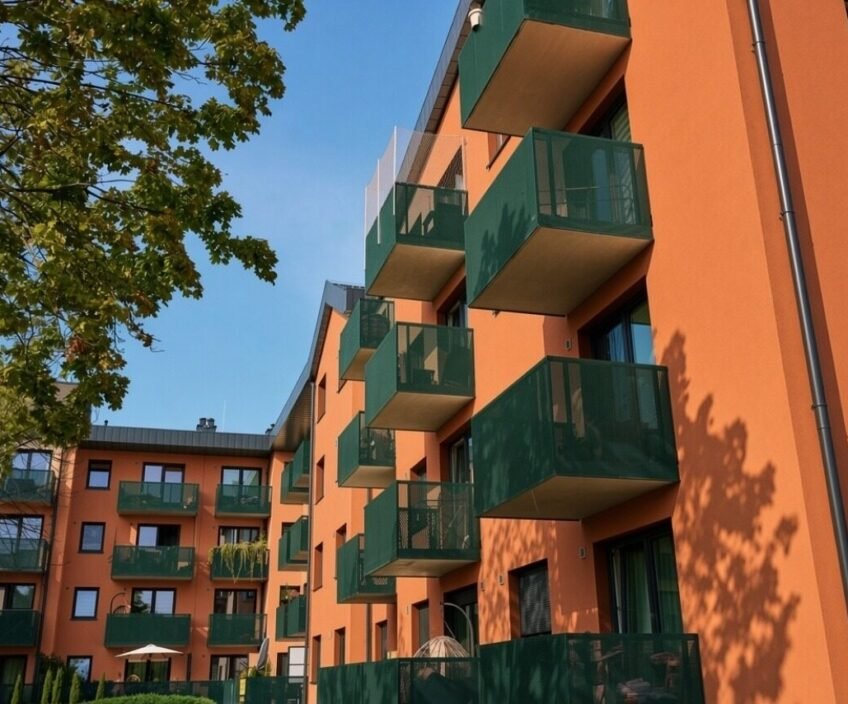 Modern orange building with green balconies and clear sky.