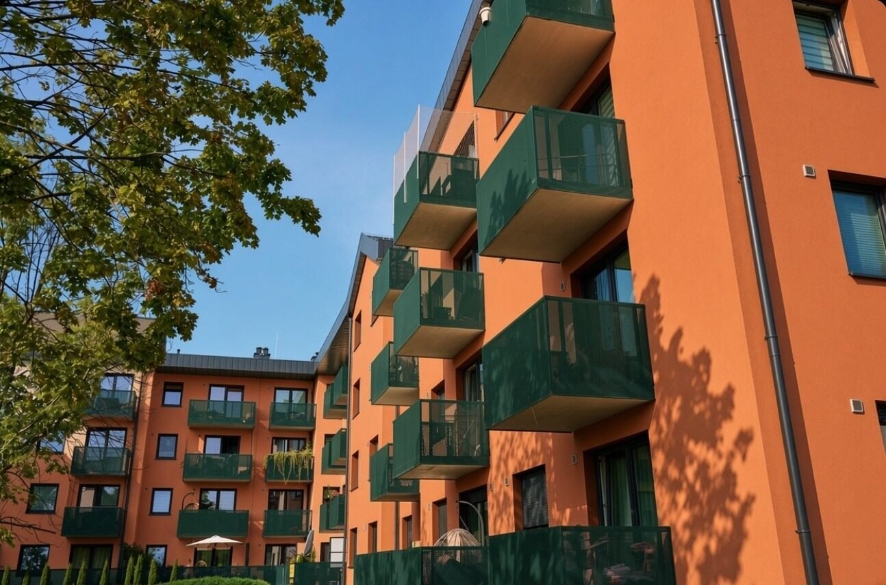 Modern orange building with green balconies and clear sky.