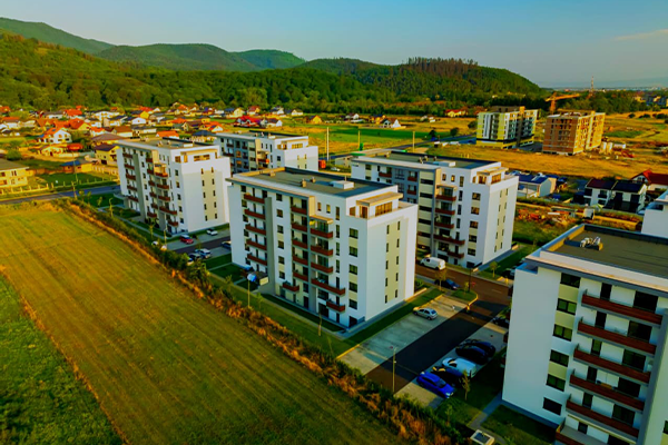 Aerial view of modern apartment buildings by a leading real estate development advisory in Kenya, surrounded by green fields and hills, with smaller houses and construction visible under a clear blue sky.